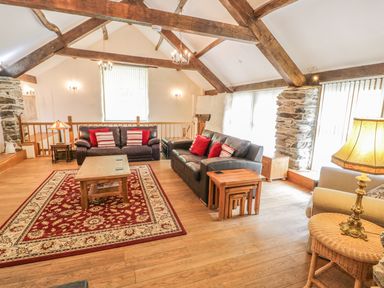 A living room with exposed wooden beams two leather sofas a wooden coffee table and a patterned rug at Hendoll Barn Friog near Fairbourne