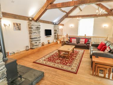 A living room with wooden beams on the ceiling two leather sofas a coffee table and a patterned area rug at Hendoll Barn Friog near Fairbourne