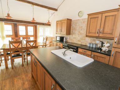 A kitchen with wooden cabinets a black countertop a white sink and a wooden dining table with chairs at Hendoll Barn in Friog near Fairbourne
