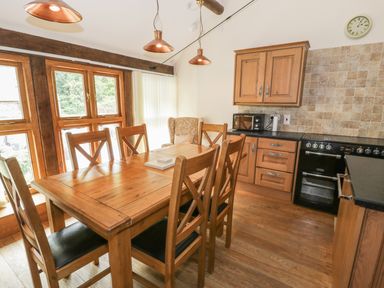A dining area with a wooden table and chairs next to kitchen cabinets and an oven at Hendoll Barn in Friog near Fairbourne