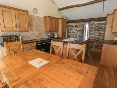A kitchen with wooden cabinets a wooden dining table with chairs a black stove and a stone wall at Hendoll Barn Friog near Fairbourne