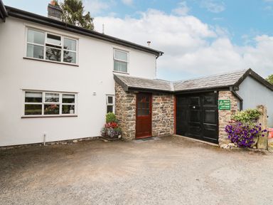 Exterior of a two story house with white walls stone entrance and black garage doors with flowers in planters at Holly Farm Cottage in Howey
