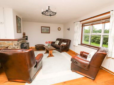 A living room with leather sofas a wooden coffee table a stone fireplace and a large window at Holly Farm Cottage in Howey
