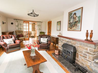 A living room with leather armchairs wooden table flowers and a stone fireplace at Holly Farm Cottage in Howey