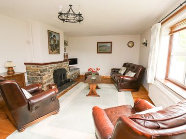 A living room with leather armchairs and a sofa a wooden coffee table a stone fireplace and a window with curtains at Holly Farm Cottage in Howey