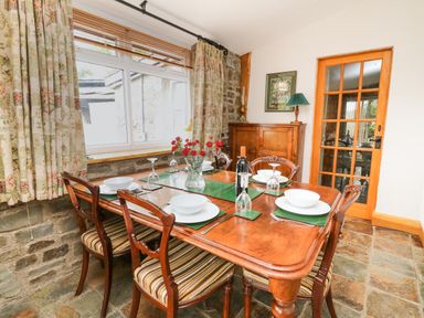 A dining room with a wooden table set with bowls and glasses and six chairs at Holly Farm Cottage in Howey