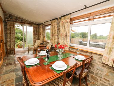 A dining area with a wooden table set for four and armchairs near windows at Holly Farm Cottage in Howey