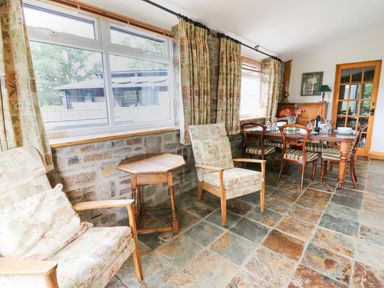 A seating area with two armchairs a wooden table and a dining table set with chairs and tableware at Holly Farm Cottage in Howey