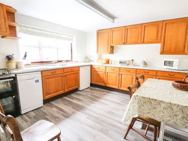 A kitchen with wooden cabinets a dining table and chairs dishwasher microwave and window at Holly Farm Cottage in Howey