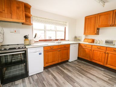 A kitchen with wooden cabinets a dishwasher a stove sink and a window at Holly Farm Cottage in Howey