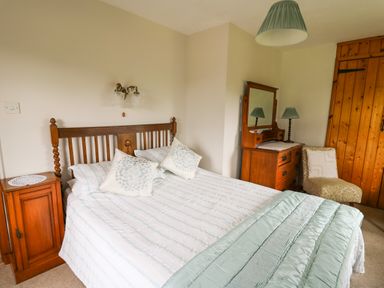 A bedroom with a wooden bed and a chest of drawers with a mirror at Holly Farm Cottage in Howey