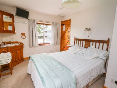 A bedroom with a double bed a wooden headboard a bedside table a window with curtains and a wooden door at Holly Farm Cottage in Howey