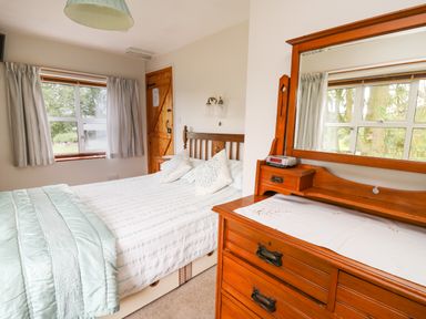 A bedroom with a bed and pillows next to a wooden dresser with a mirror at Holly Farm Cottage in Howey