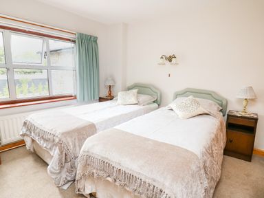 A bedroom with two single beds side by side with cushions and throws bedside tables with lamps and a window with curtains at Holly Farm Cottage in Howey