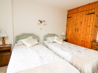 A bedroom with two single beds a wooden wardrobe and bedside tables with lamps at Holly Farm Cottage in Howey