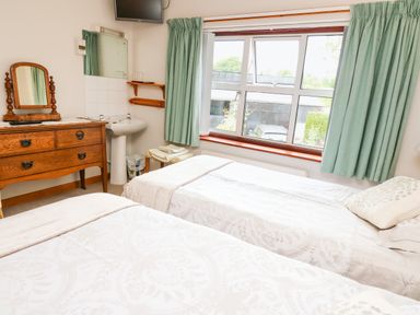 A bedroom with two single beds a wooden dresser with a mirror a sink and a window with green curtains at Holly Farm Cottage in Howey