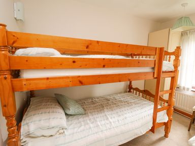 A wooden bunk bed with striped bedding and a green pillow in a bedroom with a window and a green lampshade at Holly Farm Cottage in Howey
