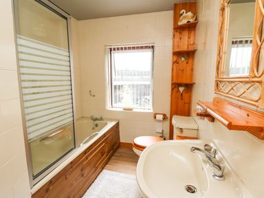 A bathroom with a bathtub wooden paneling toilet and sink with wooden shelves and mirror at Holly Farm Cottage in Howey