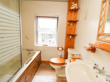 A bathroom with a bathtub with wooden paneling a toilet with wooden seat a sink and a wooden shelving unit at Holly Farm Cottage in Howey