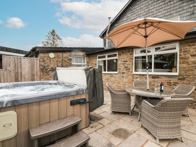 An outdoor patio with a hot tub a round glass table with four wicker chairs and a large umbrella at Holly Farm Cottage in Howey