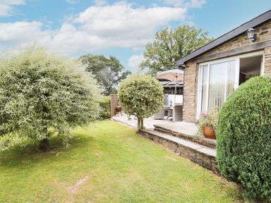 A garden with trimmed bushes and a stone patio outside a house at Holly Farm Cottage in Howey