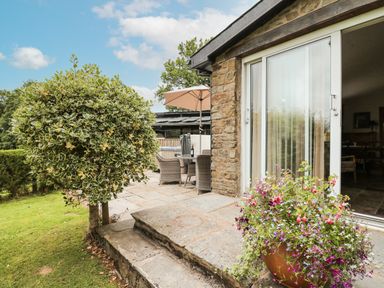 Stone patio with potted flowers and outdoor dining set next to sliding glass doors at Holly Farm Cottage in Howey