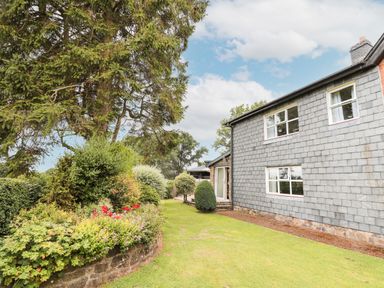 An outdoor garden area with bushes flowers and a large tree next to a two story house at Holly Farm Cottage in Howey