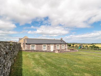 A single-storey brick house with windows and a door surrounded by grass and a stone wall at Grey Croft in Embleton