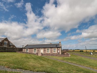 A stone building with a slate roof on a grassy lawn under a partly cloudy sky at Grey Croft in Embleton