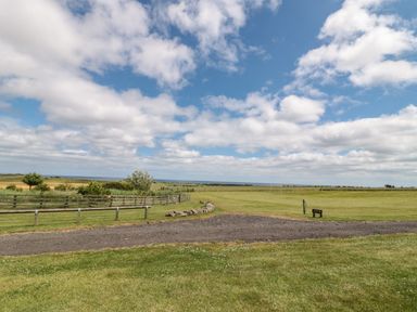 A grassy field with a dirt path and fences under a cloudy sky at Grey Croft in Embleton
