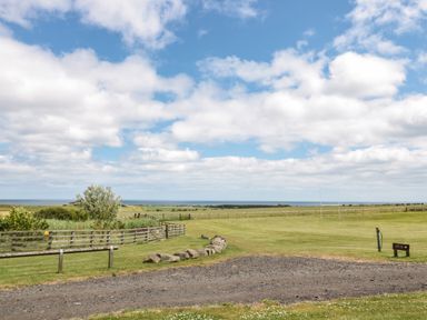 An open grassy field with a gravel path wooden fences and a distant view of the sea at Grey Croft in Embleton