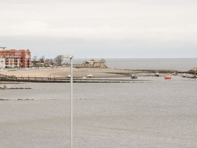 A coastal scene with boats on the water buildings along the shore and a beach at Treetops in Rhos-On-Sea
