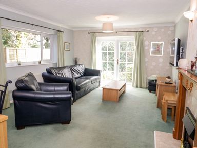 A living room with black leather sofas a wooden coffee table a wall-mounted television and French doors at Treetops in Rhos-On-Sea