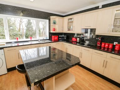 A kitchen with black countertops light wood cabinets and red accessories at Treetops in Rhos-On-Sea