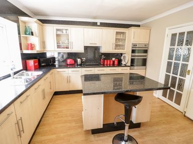 A kitchen with wooden cabinets black countertops a black stool and kitchen appliances at Treetops in Rhos-On-Sea