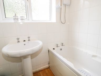A bathroom with a white sink pedestal and a white bathtub with shower at Treetops in Rhos-On-Sea