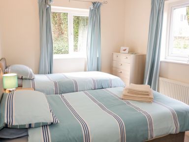 A bedroom with two single beds with blue striped bedding a chest of drawers and blue curtains at Treetops in Rhos-On-Sea