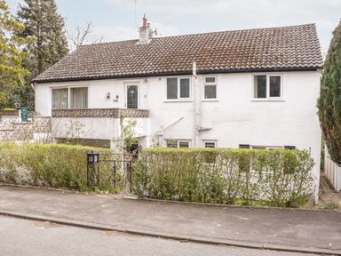 A two story white house with a tiled roof surrounded by trees and a hedge at Treetops in Rhos-On-Sea