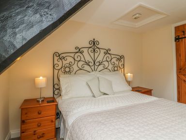 A bedroom with a bed with an ornate metal headboard and wooden nightstands with lamps at Fig Trees - Wibble Farm in Williton near Watchet