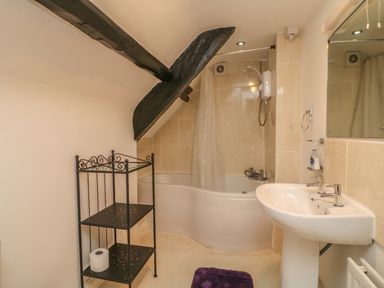 A bathroom with a bathtub a shower a sink a black metal shelf and a purple bath mat at Fig Trees - Wibble Farm in Williton near Watchet