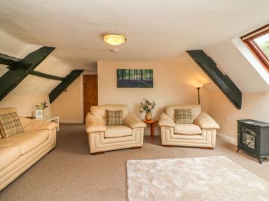A living room with two armchairs and a sofa with cushions a small wooden table with flowers a standing lamp and a heater by the window at Fig Trees - Wibble Farm in Williton near Watchet