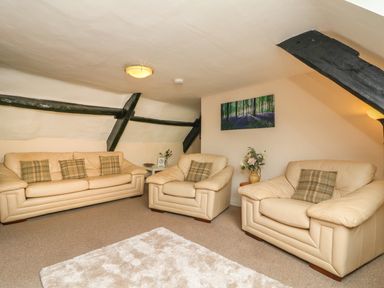 A sitting room with beige leather sofas and armchairs with cushions a white rug on the floor and wall art at Fig Trees - Wibble Farm in Williton near Watchet