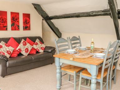 A dining table set for four beside a sofa with cushions under a sloped ceiling with black beams at Fig Trees - Wibble Farm in Williton near Watchet