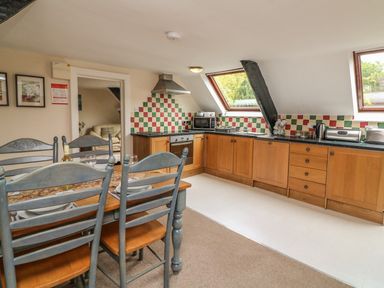 A kitchen and dining area with wooden cabinets a dining table with chairs and colorful tiled backsplash at Fig Trees - Wibble Farm in Williton near Watchet