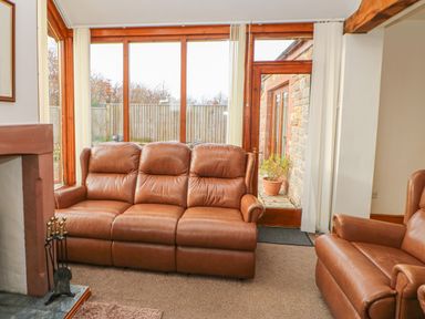 A living room with leather sofas a fireplace and large windows at Swallow Cottage in Milton near Brampton