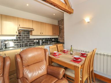 A dining area with wooden table and chairs set with bowls and glasses next to a kitchen with wooden cabinets and black tiled backsplash at Swallow Cottage in Milton near Brampton