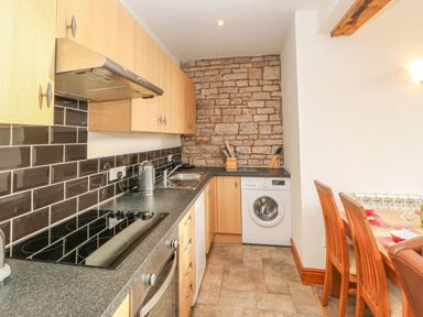 A kitchen with wooden cabinets black tiled backsplash a stovetop oven washing machine and wooden dining chairs at Swallow Cottage in Milton near Brampton