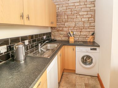 A kitchen with wooden cabinets black countertops a stainless steel sink a washing machine and a kettle at Swallow Cottage in Milton near Brampton