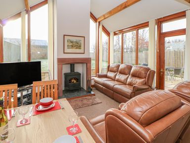 A living room with leather sofas a wood burning stove a dining table and large windows at Swallow Cottage in Milton near Brampton