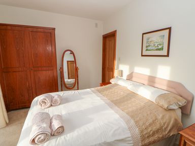 A bedroom with a double bed towels on the bed and a wooden wardrobe with a mirror at Swallow Cottage in Milton near Brampton